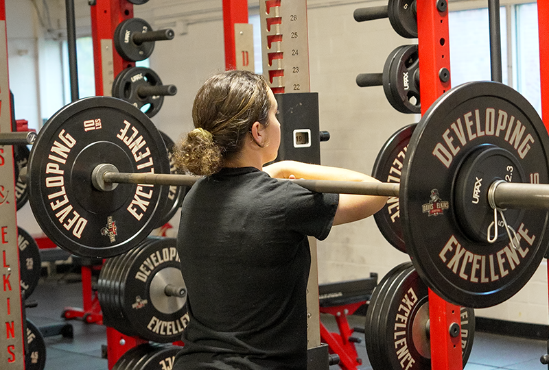 women's softball player squatting a barbell and weights in Martin weightroom